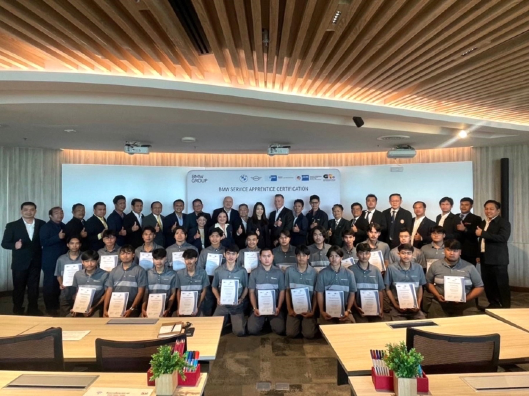 Apprentices holding their certificates at a BMW Service Apprentice certification, with GTCC and partner marks on the backdrop.
