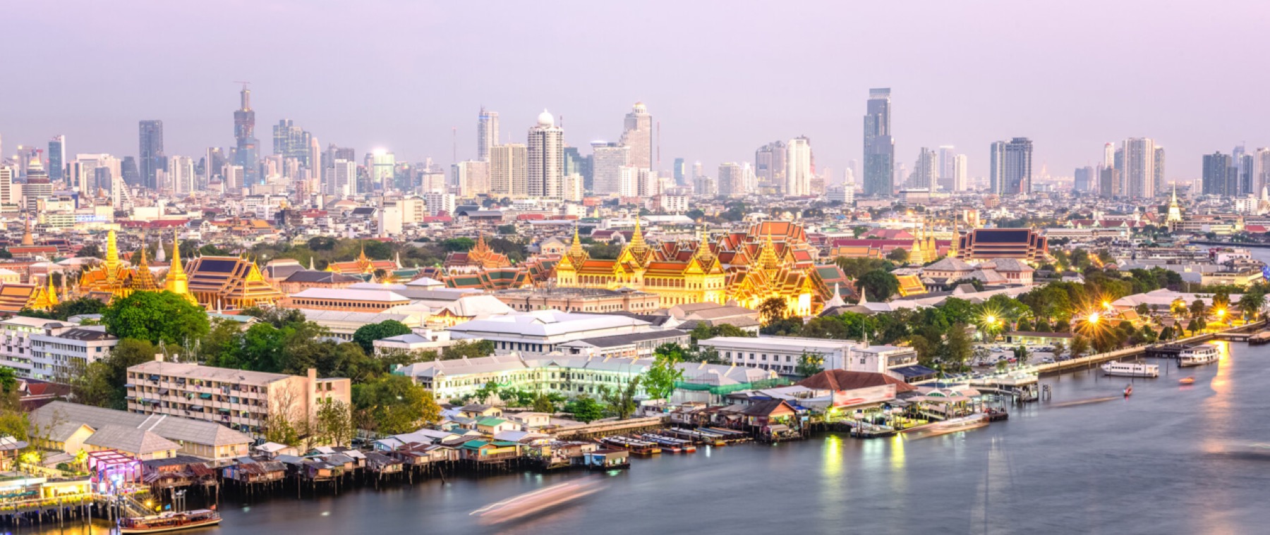 The Bangkok skyline at dusk over the Chao Phraya, with the Grand Palace lit in the foreground.